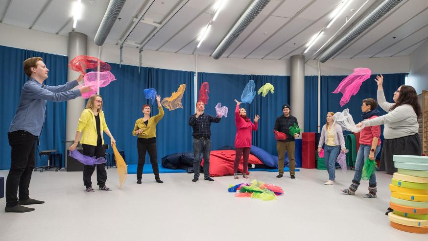 Toimintaterapian opiskelijat ja opettajat heittävät värikkäitä huiveja ilmaan aistihuoneessa.