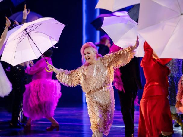 Leena Liimatainen esiintyy sateenvarjo kädessä muiden esiintyjien seassa.