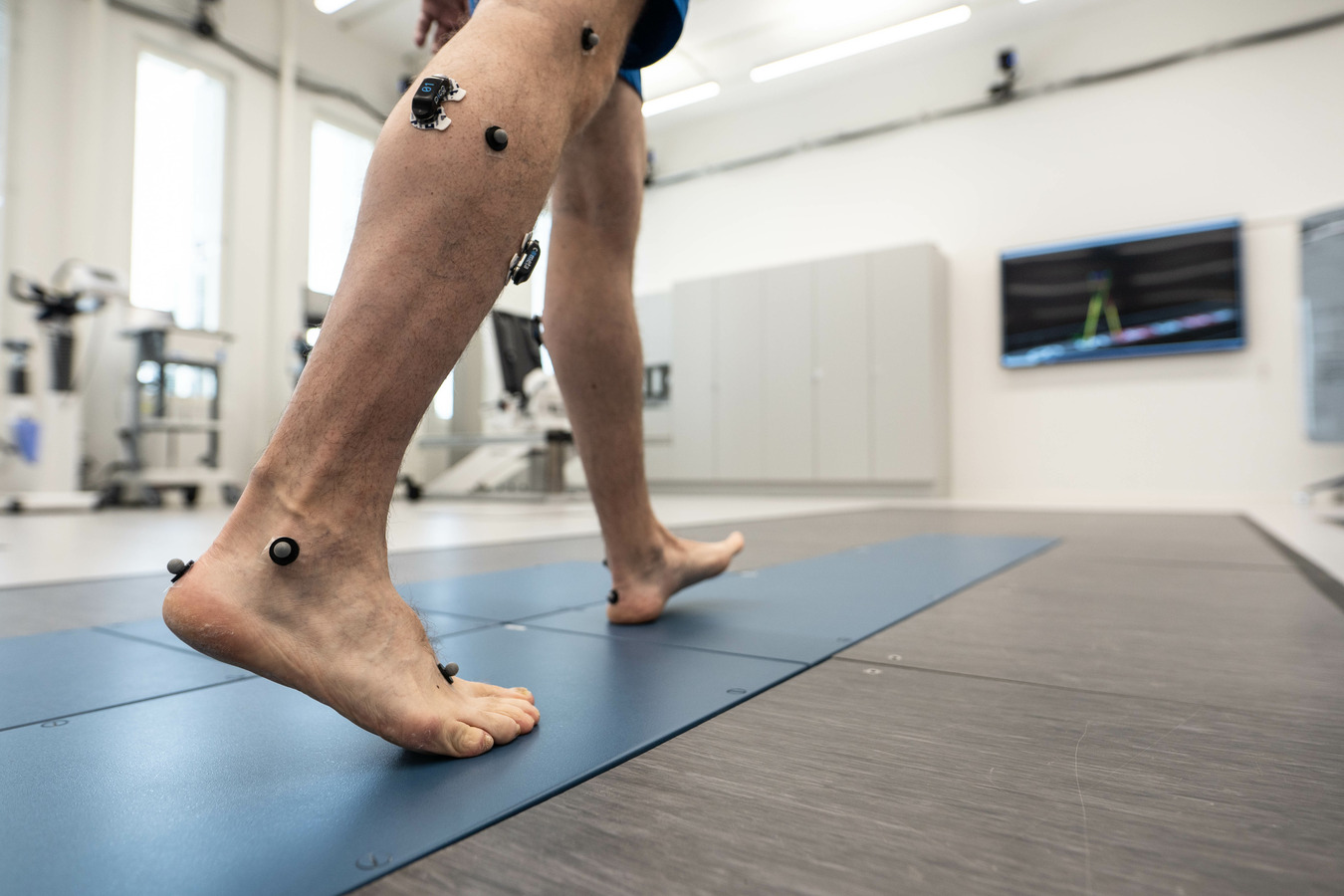 Man walking barefeet on force platform, wearing reflective markers and muscle activity equipment.