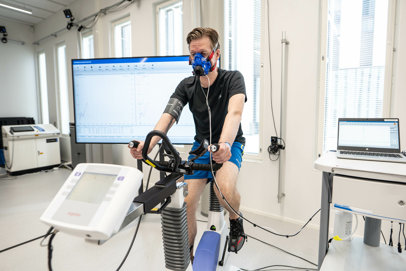 Mies istuu polkupyöräergometrin päällä, kasvoilla hengityskaasuanalysaattorin maski, josta kulkee piuha hengityskaasuanalysaattoriin.