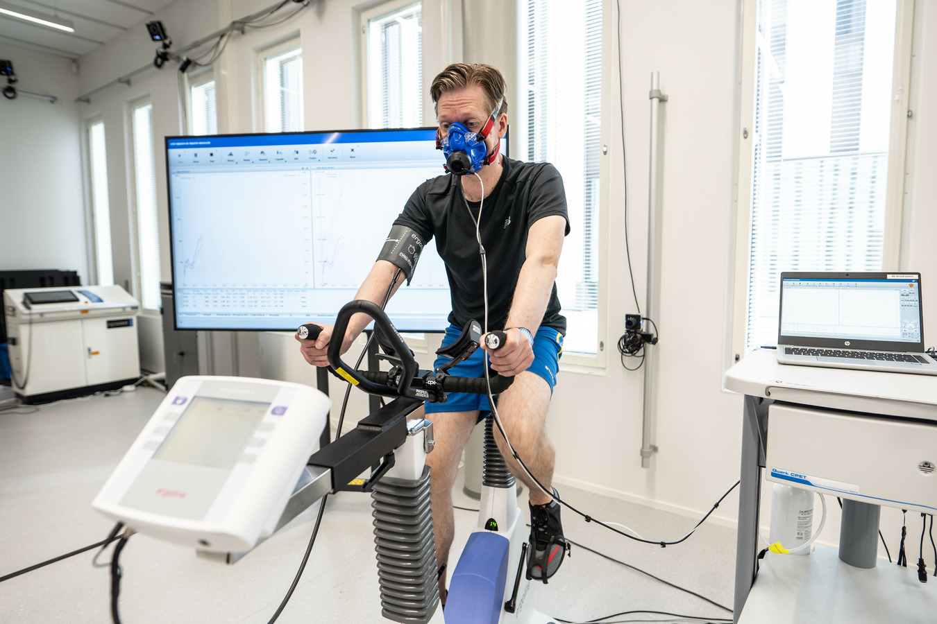 Man sitting on cycle ergometer wearing respiratory face mask.