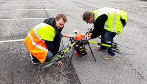 Kaksi opiskelijaa, joilla on yllään huomioliivit, laittavat maanmittauksen opinnoissa käytettävää dronea toimintakuntoon ulkona.