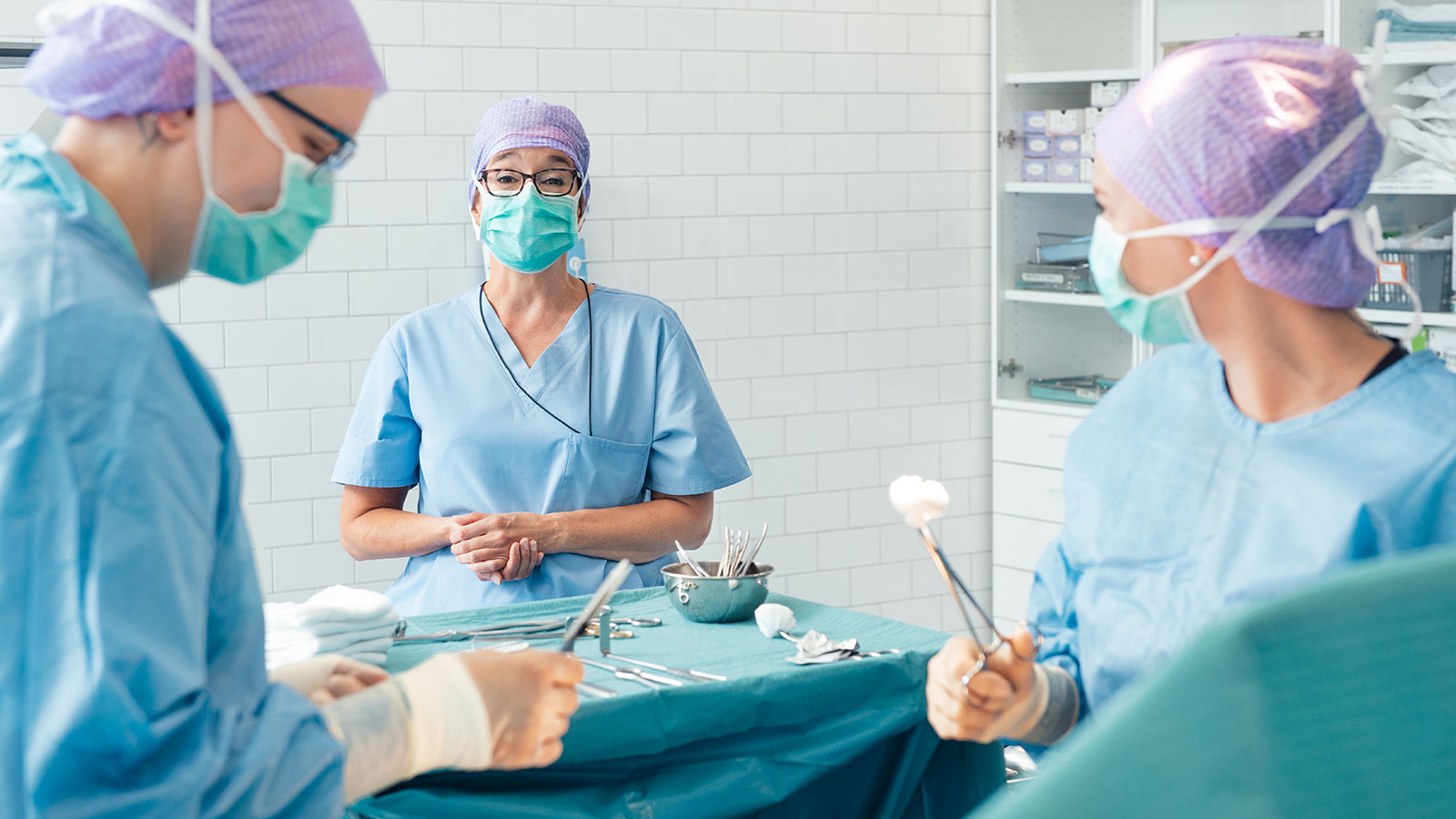 Teacher guiding two nursing students in operation simulation.
