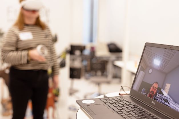 Taustalla henkilö kokeilemassa VR-simulaatiolaseja ja kuvassa etualalla läppärin ruudulla "potilas".