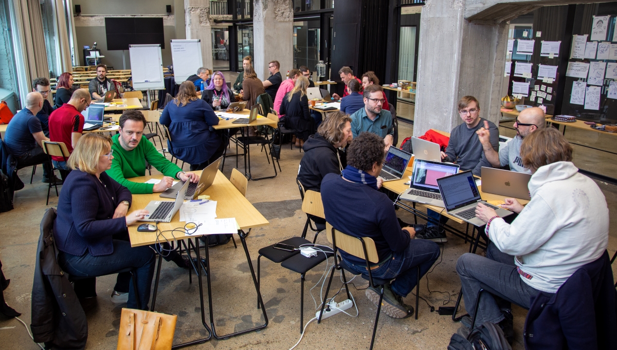 People seated in a classroom setting around tables, workshopping.