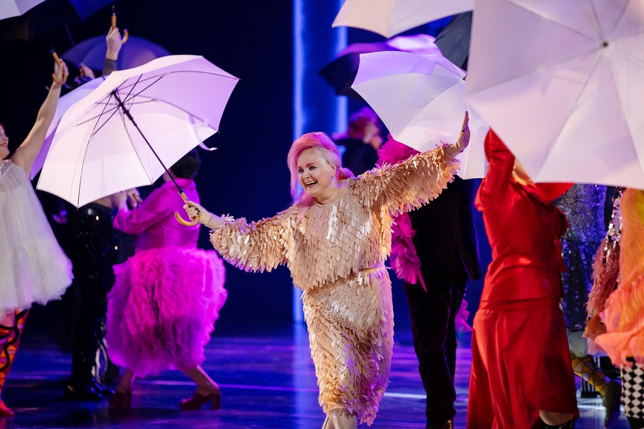 Leena Liimatainen esiintyy sateenvarjo kädessä muiden esiintyjien seassa.