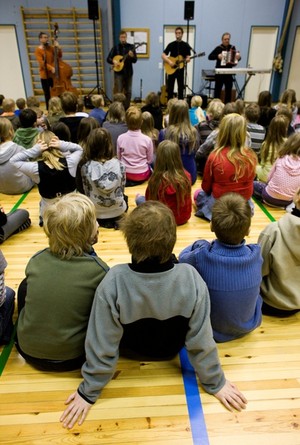 Opiskelijoista koostuva yhtye soittaa alakouluikäiselle yleisölle koulun liikuntasalissa.