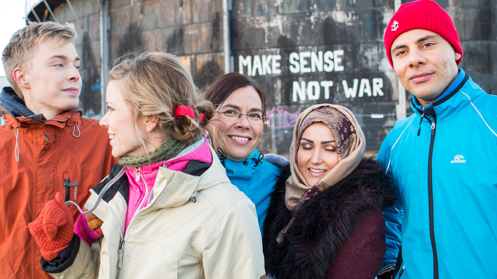 Viisi henkilöä Make sense not war -seinäkirjoituksen edessä.