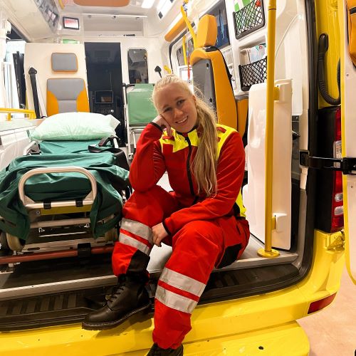 Ensihoitajaopiskelija Hanna Luoto istumassa ambulanssin takaosassa, jossa auton ovet avoinna.