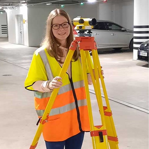 Maanmittaustekniikan opiskelija Milla Aaltonen parkkihallissa mittauslaitteen kanssa.