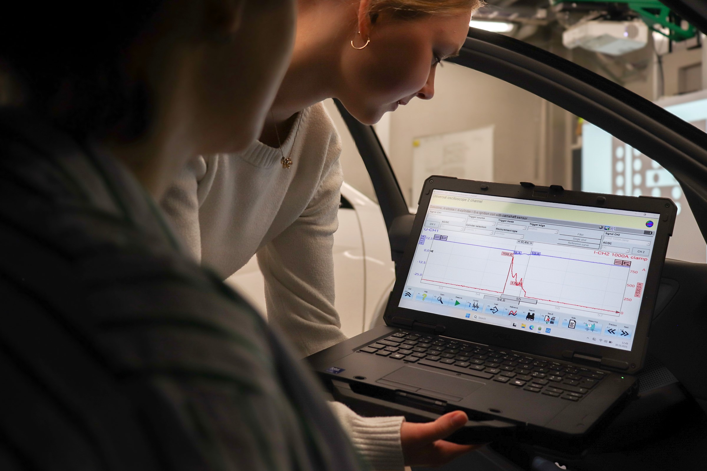 Two students in a car reading measurements from a laptop computer
