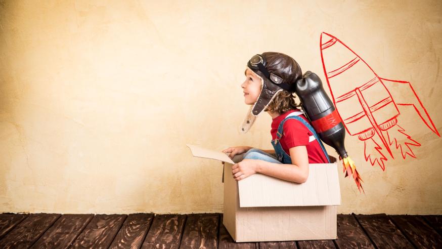 Lapsi istuu kypärä päässä pahvilaatikossa, taustalla olevalle seinälle piirretty raketti.