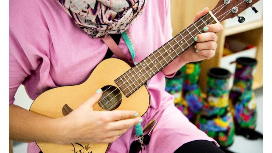Ukulelen soittaja istuu ukulele sylissään.