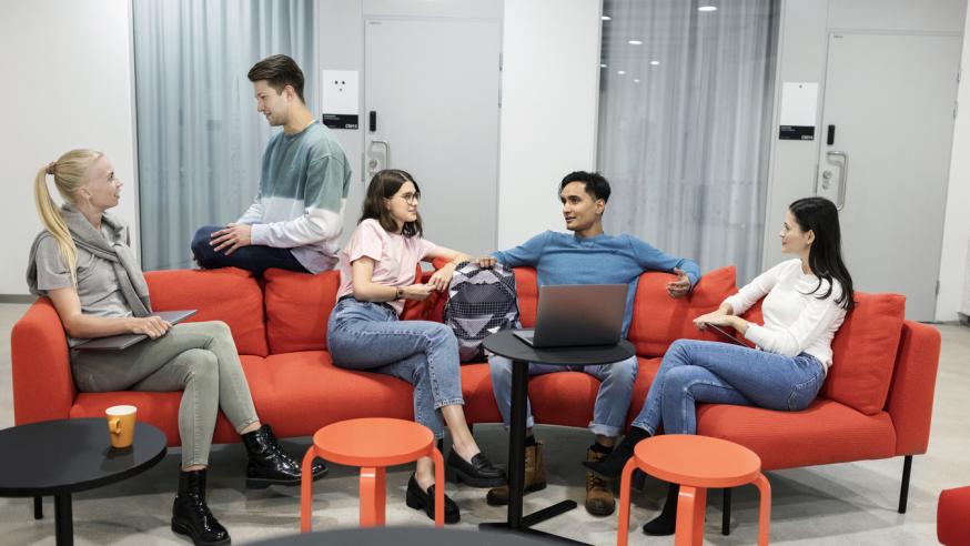 Group of young people sitting in lounge, 2 in the back talking to each other and 3 in front tqalking to each other