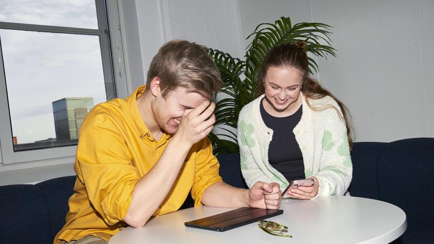 kaksi opiskelijaa pöydän ääressä nauramassa