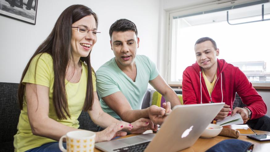 Kolme opiskelijaa keskustee tietokoneen äärellä