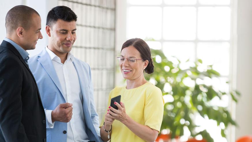 Three people discussing, one is showing something on her cellphone.