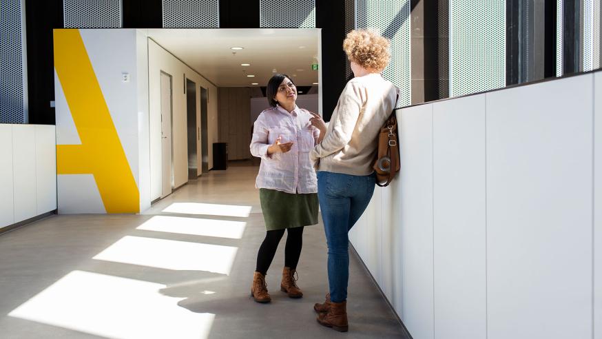 Kaksi opiskelijaa keskustelee kampuksen käytävällä.