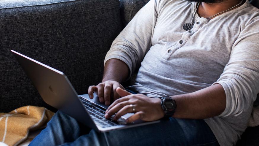 Student sitting on the sofa a laptop on his lap.