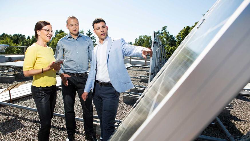Kolme henkilöä tutkii aurinkopaneeleja kampuksen katolla.