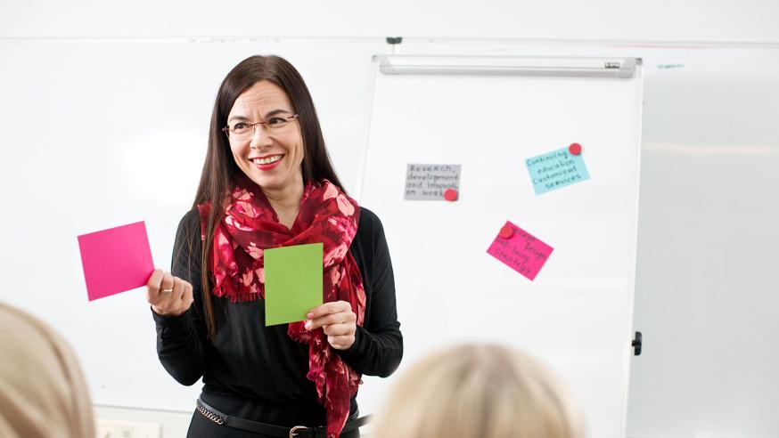 Opettaja seisoo fläppitaulun edessä ja pitää post-it-lappuja käsissään..
