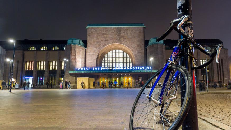 Helsingin rautatieaseman pääsisäänkäynti ja sen edustalle tolppaan kiinnitetty polkupyörä.