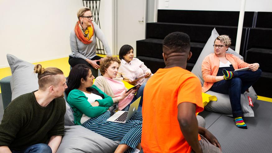 Six students discussing and sitting on bean bags, teacher on back.