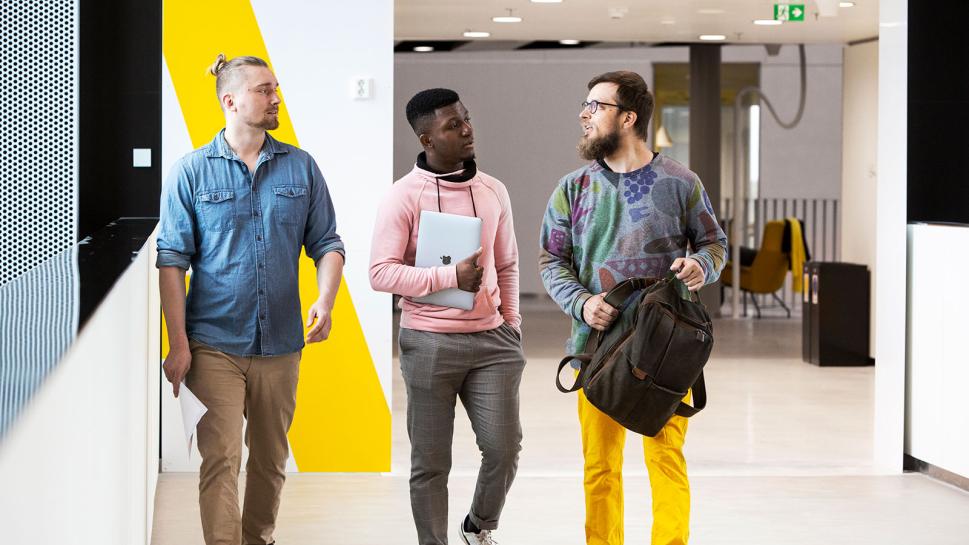 Three people discussing while walking in the campus corridor.