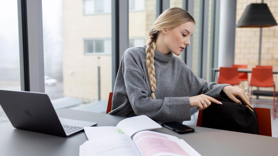 Student sitting by a laptop and notes and going through her packbag.