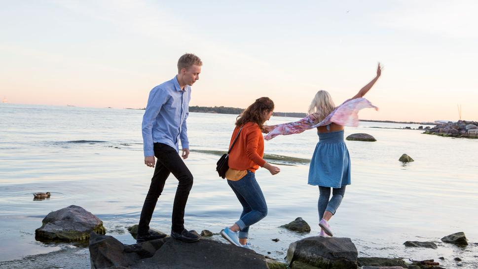 Kolme henkilöä kävelee rantakallioilla.