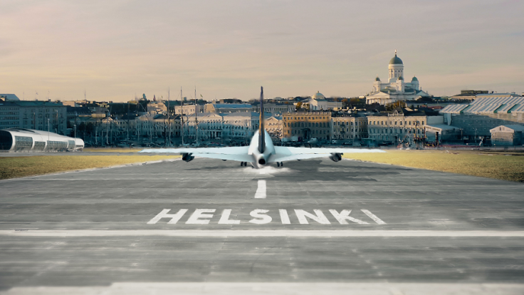An airplane taking off, situated in middle of image, on ground text Helsinki, in the background cropped Helsinki city center skyline from the sea