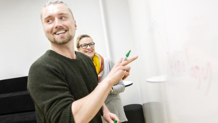 Kaksi henkilöä suunnittelevat valkotaulun edessä.