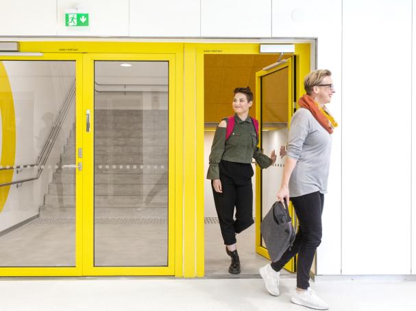 Kaksi naishahmoa poistumassa keltaisista ovista.