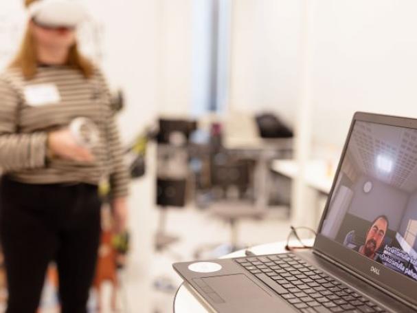 Taustalla henkilö kokeilemassa VR-simulaatiolaseja ja kuvassa etualalla läppärin näytöllä "potilas".