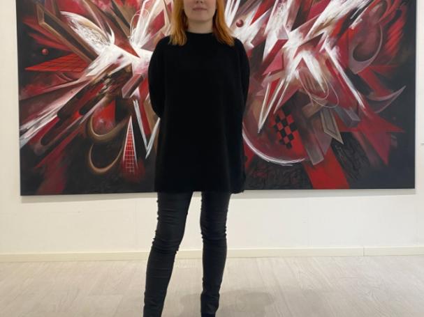 Muotoilun alumni Matilda Hööpakka mustissa vaatteissa kuvattuna punamustavalkoisen taideteoksen edessä.
