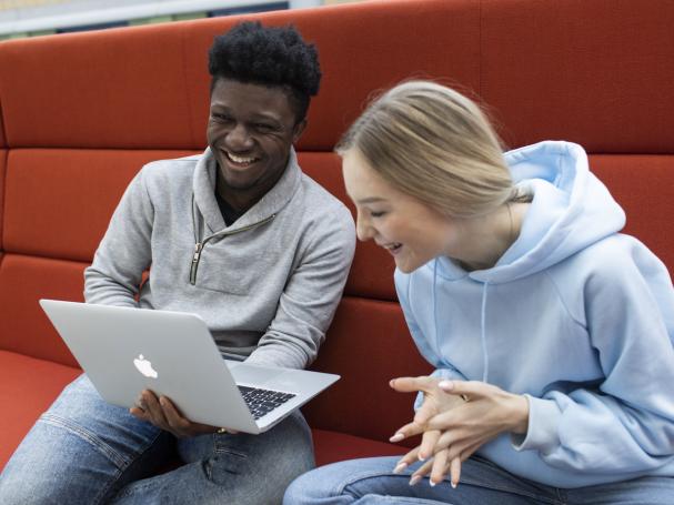 Kaksi opiskelijaa nauraa yhdessä tietokoneen äärellä.