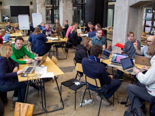 People seated in a classroom setting around tables, workshopping.