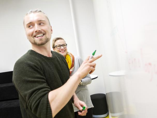 Kaksi henkilöä suunnittelevat valkotaulun edessä.