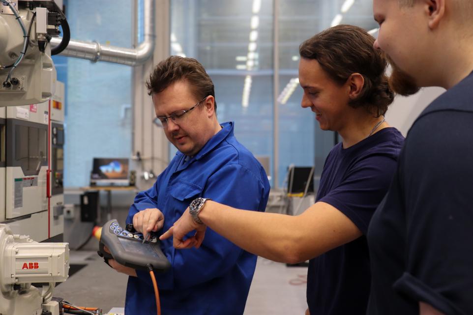 Instructor teaching two students how to use a robot arm controller