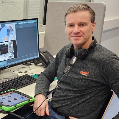 Speaker Ari-Pekka Åker sitting by computer desk looking at the camera.