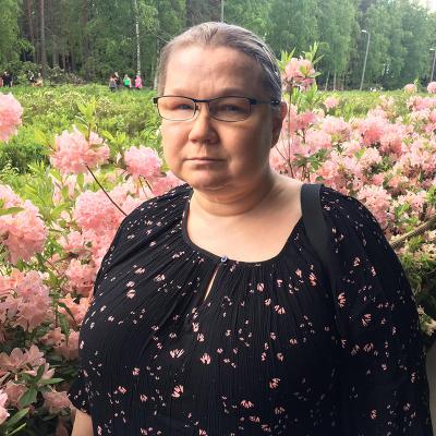 Speaker Inka Koskivirta standing in frot of a rose bush, lookin at camera.