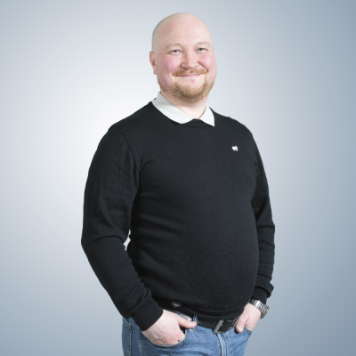 Potretissa hymyilevä Mikko Raikaa tumma neule, kauluspaita ja farkut yllään.