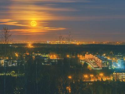 Moon rising over city, view from a hill.