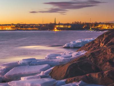 Ice covered sea, city on the horizon time of sunset.