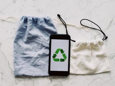 Kaksi kangaspussia ja mobiililaite, jonka näytöllä on kierrätystä kuvaava symboli.