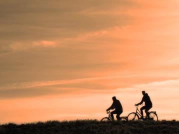 Kaksi pyöräilijää pyöräilemässä ilta- tai aamuruskon aikaan.