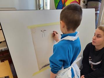 Lapsi maalaamassa taulua liituväreillä, aikuinen auttaa vieressä. 